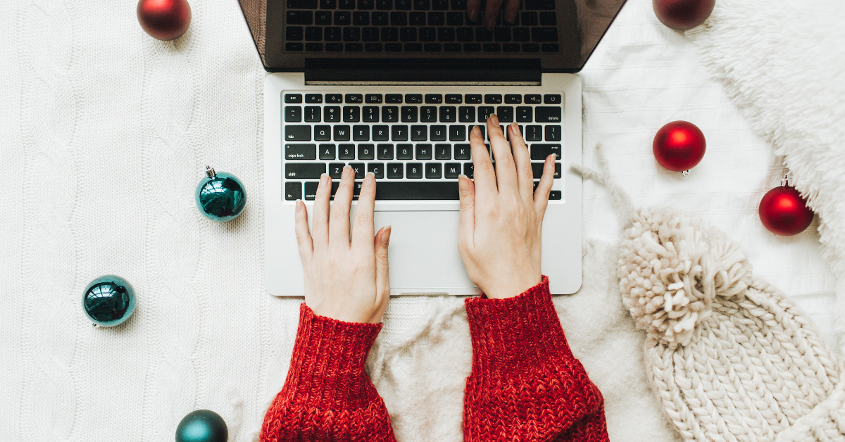 hands typing on a computer with a christmas background on the desk.